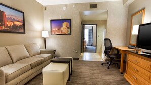 A hotel room with a sofa, a small table, a TV, a desk with a chair, and a wardrobe. - Drury Inn & Suites Lafayette, LA (Lafayette)