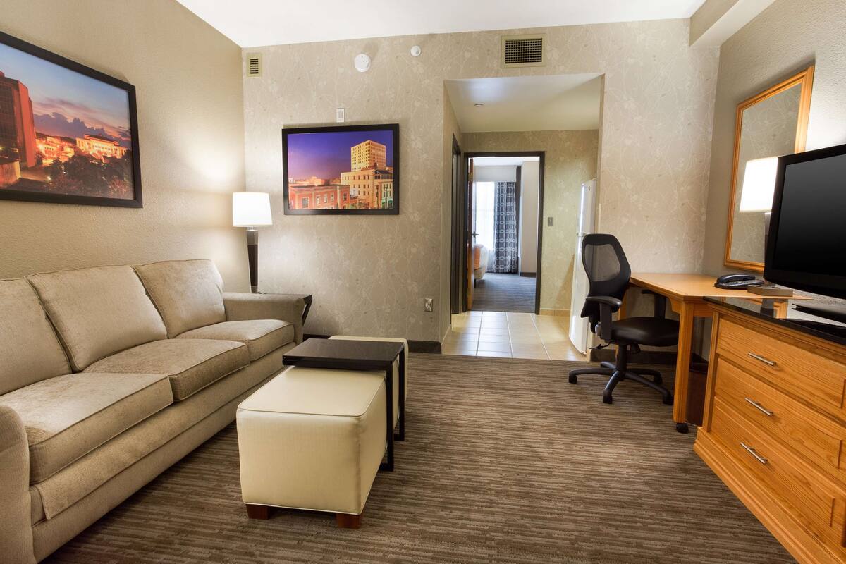 Habitación de hotel con sofá, una mesita, televisor, escritorio con silla y armario.