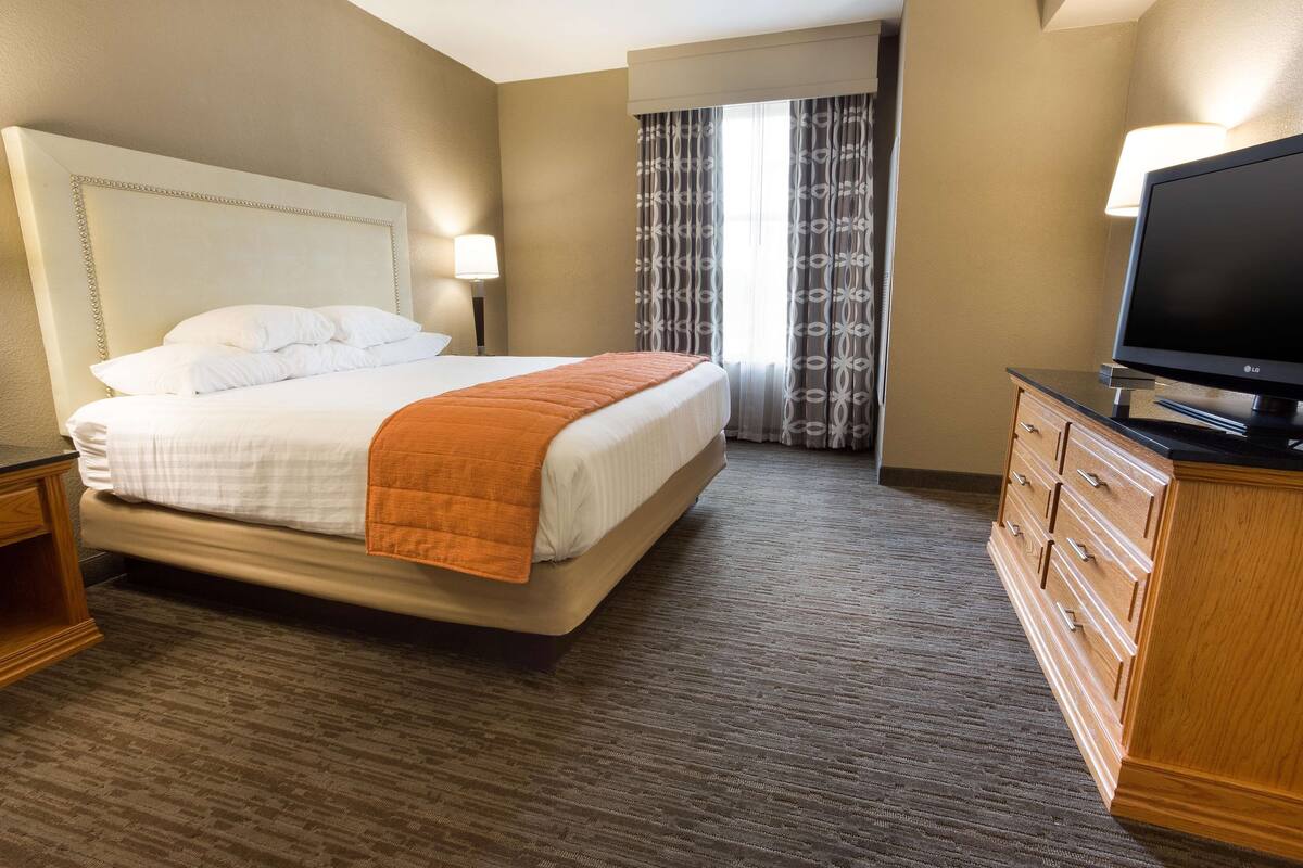 Habitación de hotel con cama, televisión, cómoda y ventana con cortinas.
