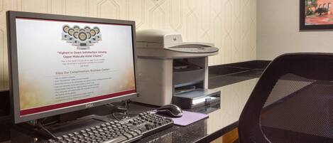 A desktop computer with a monitor displaying a customer satisfaction award, a printer, and a black office chair.