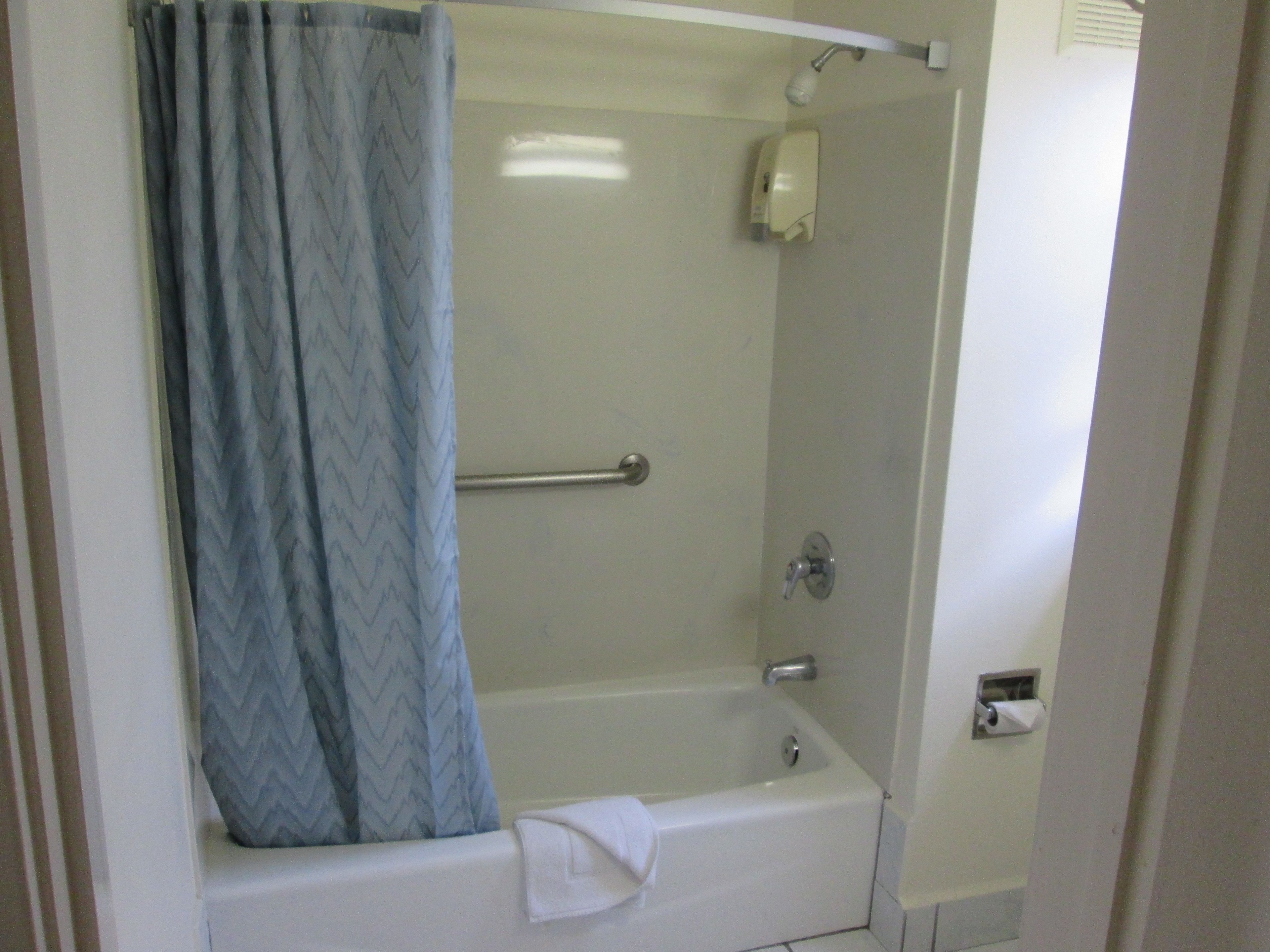 A standard white bathroom with a shower, a towel on the tub, and a hand soap dispenser.