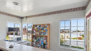 A hotel reception area with a large window, a wooden bookcase filled with travel guides, a microwave, and a small table with a bell. - Discovery Inn (Seaside)