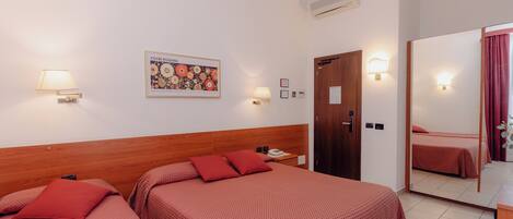 Une chambre d’hôtel avec deux lits, une tête de lit en bois, un climatiseur fixé au mur, un tableau encadré et un miroir qui reflète la pièce.