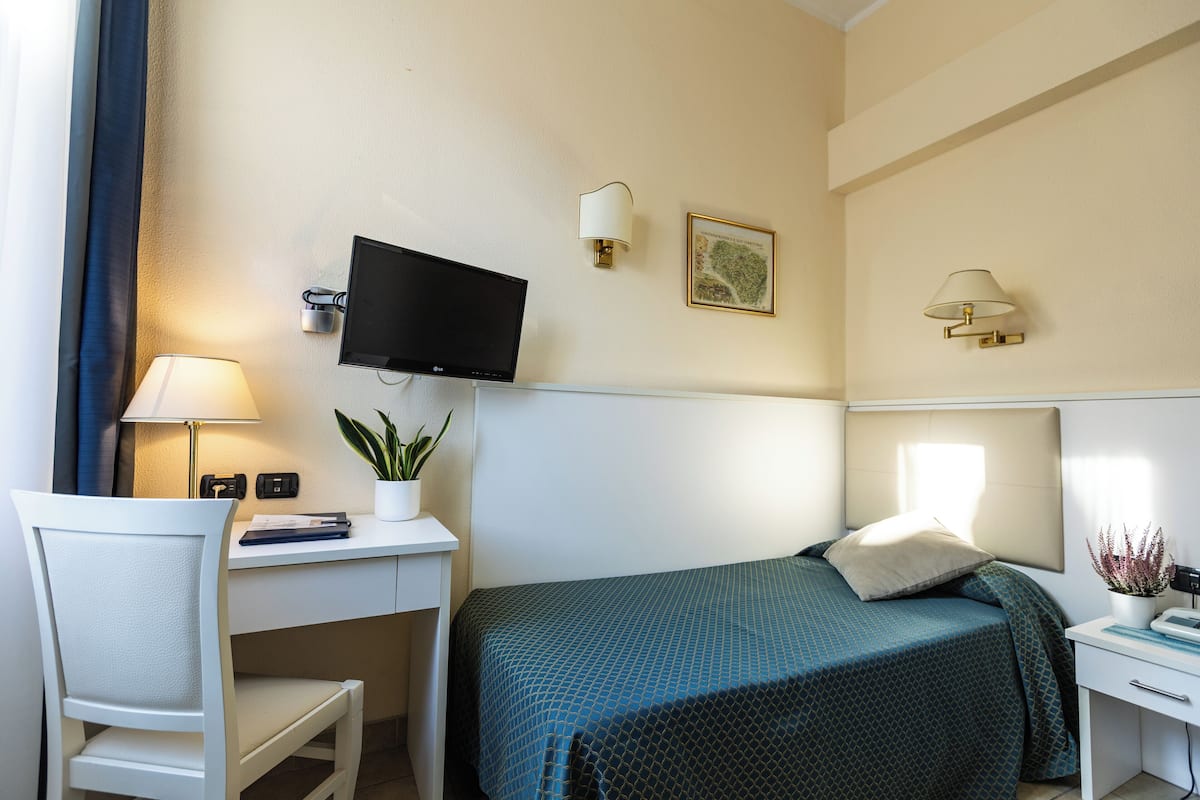 Habitación de hotel con cama, escritorio, silla, televisor, lámparas de pared y una planta en maceta.