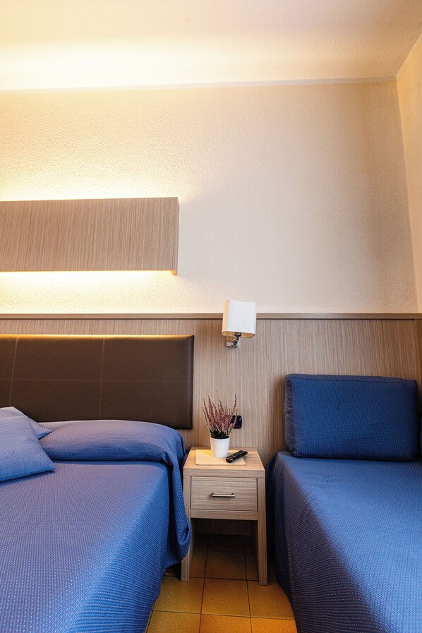 A hotel room with two beds, a bedside table with a lamp, and a small potted plant.