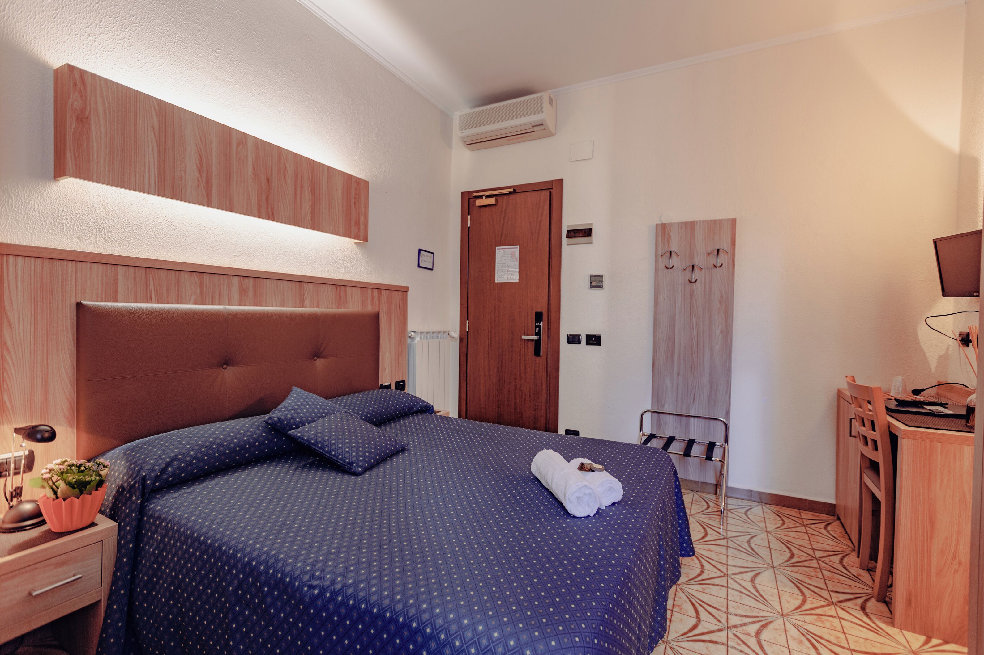 A bedroom with a large bed, a wooden headboard, a bedside table with a lamp, and a small plant.