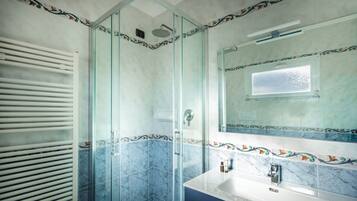 Une salle de bain dotée d’une douche à parois de verre, d’un lavabo blanc et d’un miroir orné d’une bordure de carreaux décoratifs.