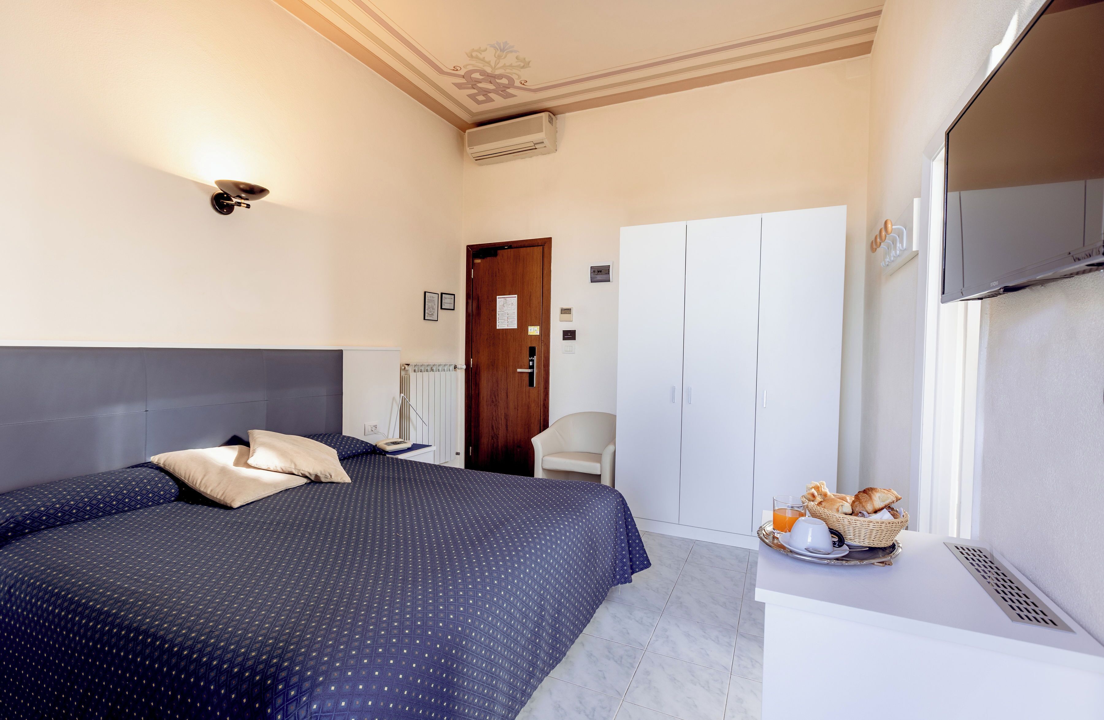 A hotel room with a bed, a desk with breakfast, a wardrobe, and a television.
