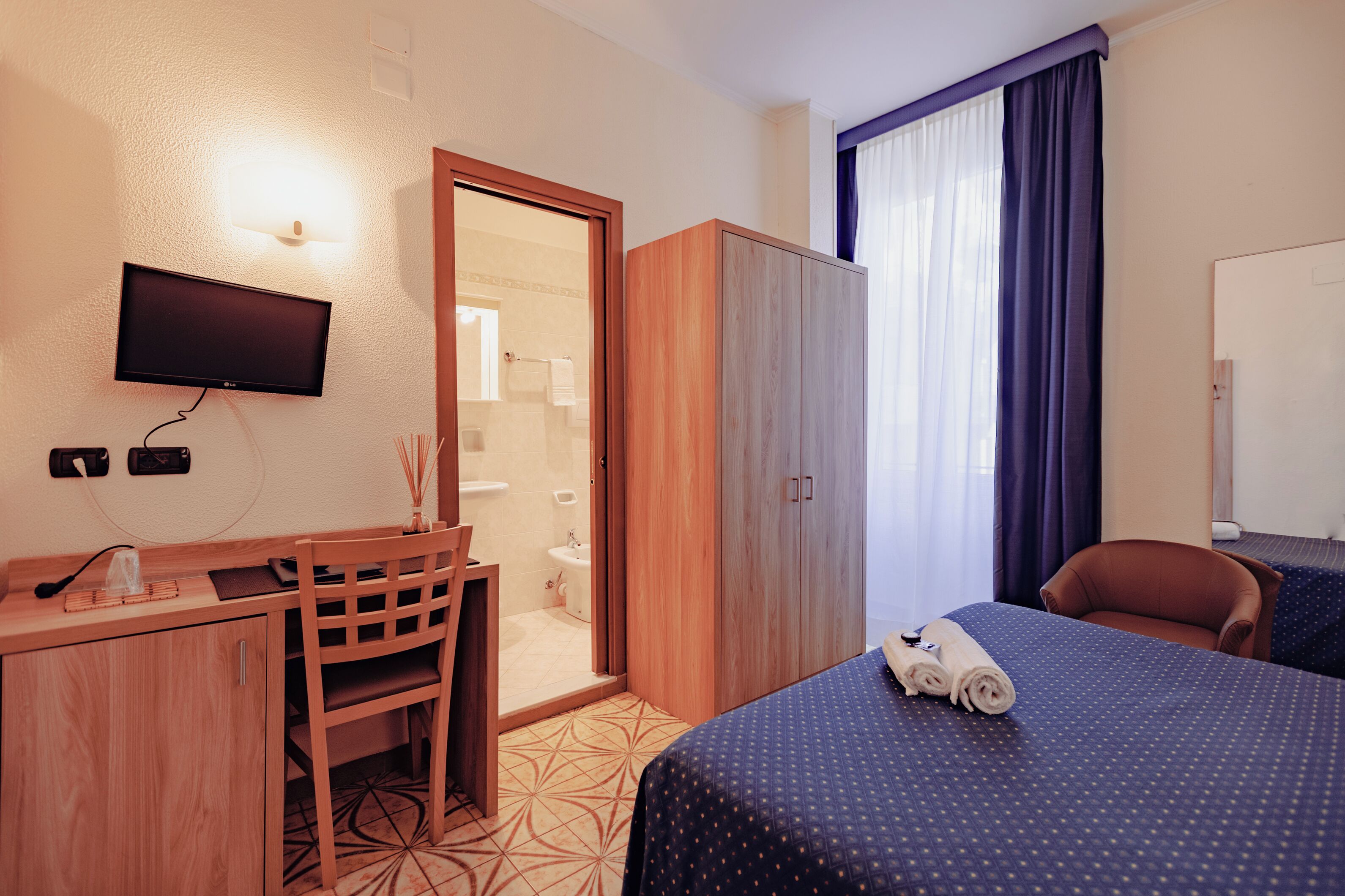 Une chambre d’hôtel comprenant un lit, un bureau, une chaise, une armoire, une télévision et une salle de bain.