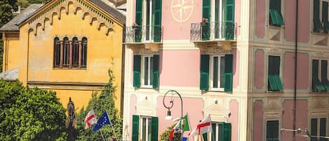 A hotel with a pink facade, green shutters, and a sign reading 'HOTEL Stella.'