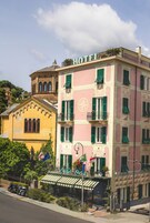 Un hotel con fachada rosa, contraventanas verdes y un letrero que dice 'HOTEL Stella'.