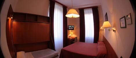 A compact hotel room with a single bed, a desk, a chair, a small table, a laptop, and a TV.