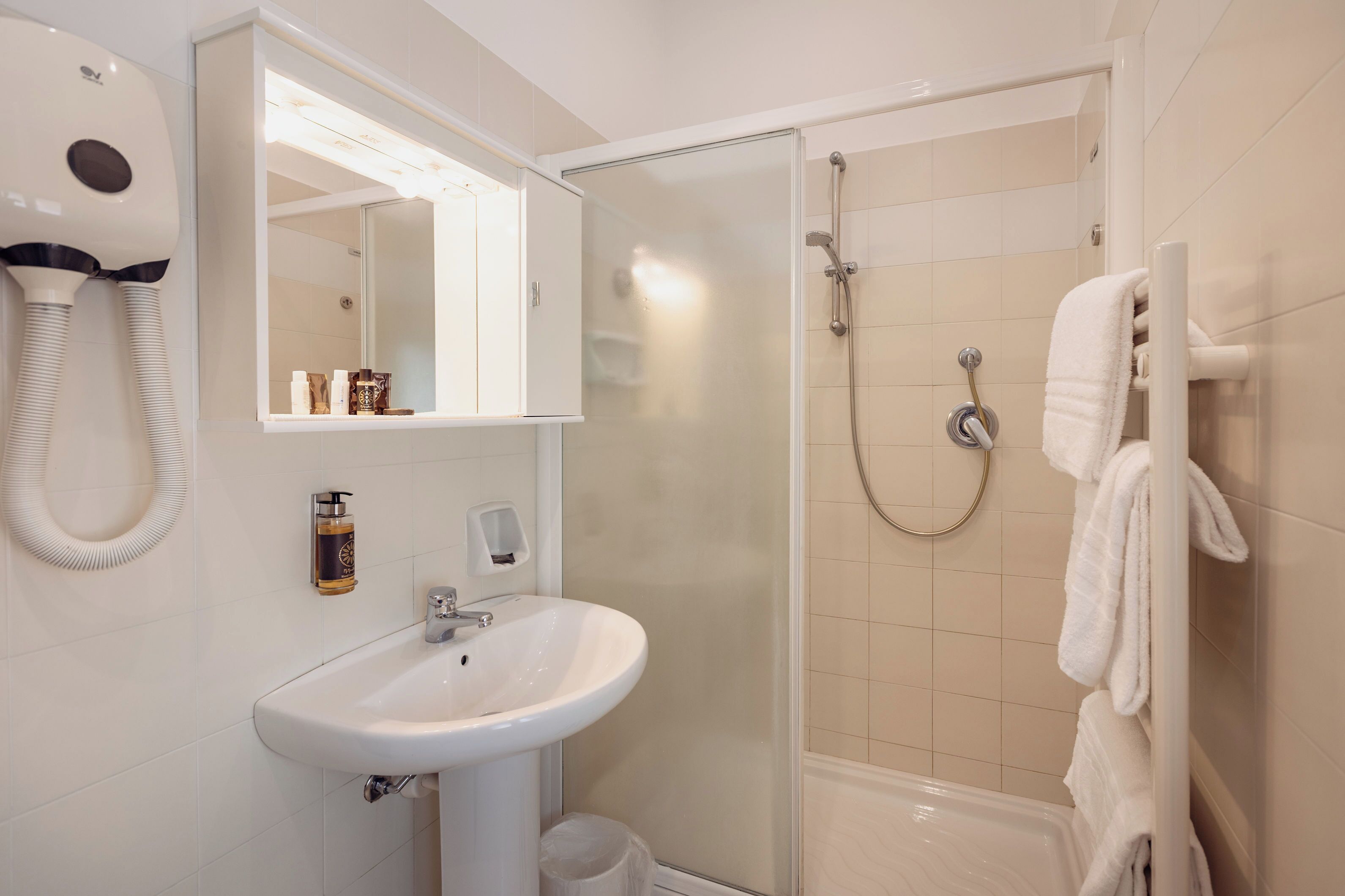 A bathroom with a white sink, a mirror, a hairdryer, a shower, and a towel rack.