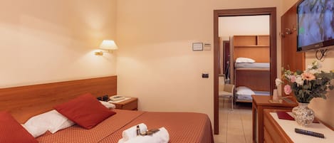 A hotel room with a bed, bedside table, TV, and a desk with a vase of flowers.