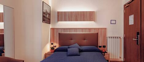 A hotel room with a large bed, a wooden headboard, a nightstand with a lamp, and a radiator.