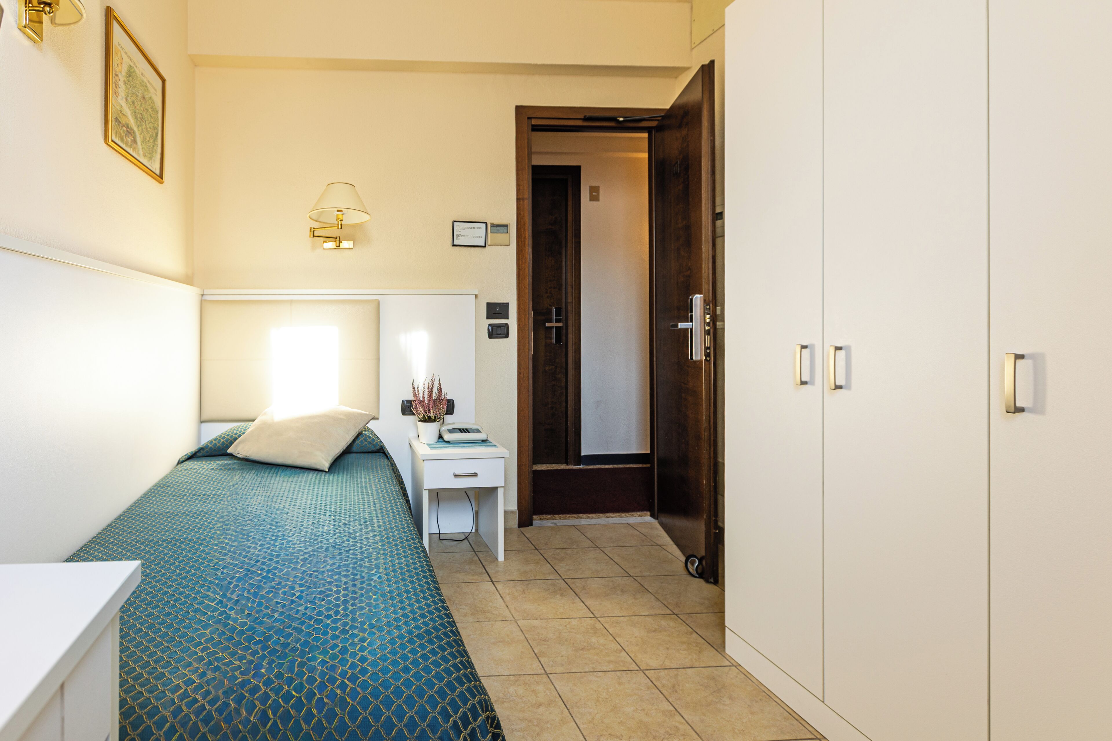 Een slaapkamer met een bed, een bureau, een stoel, een kledingkast en een deur naar een andere kamer.