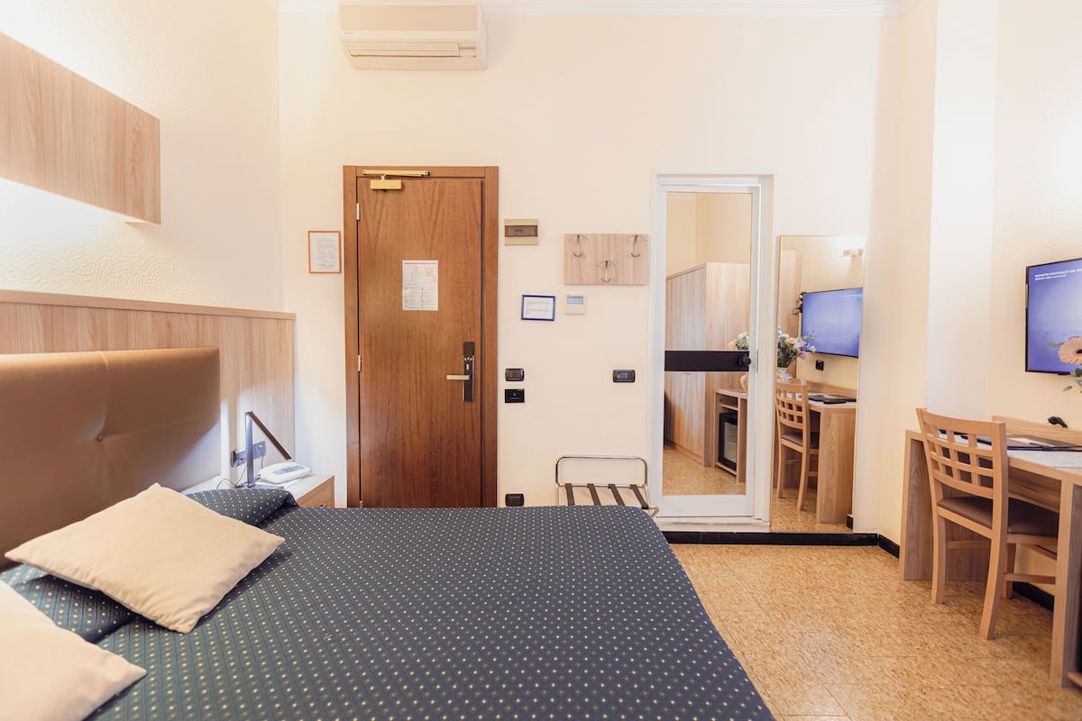 Una habitación de hotel con cama, escritorio, silla, puerta de madera y espejo.