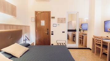 Una habitación de hotel con cama, escritorio, silla, puerta de madera y espejo.