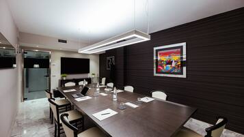 A modern conference room with a long table, chairs, a flat-screen TV, and a painting on the wall.