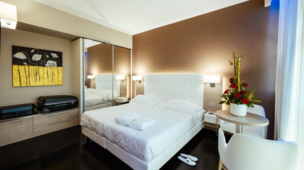 A hotel room with a large bed, a bedside table, a chair, a desk, a mirror, and a painting on the wall. - Raffaello Hotel (Senigallia)