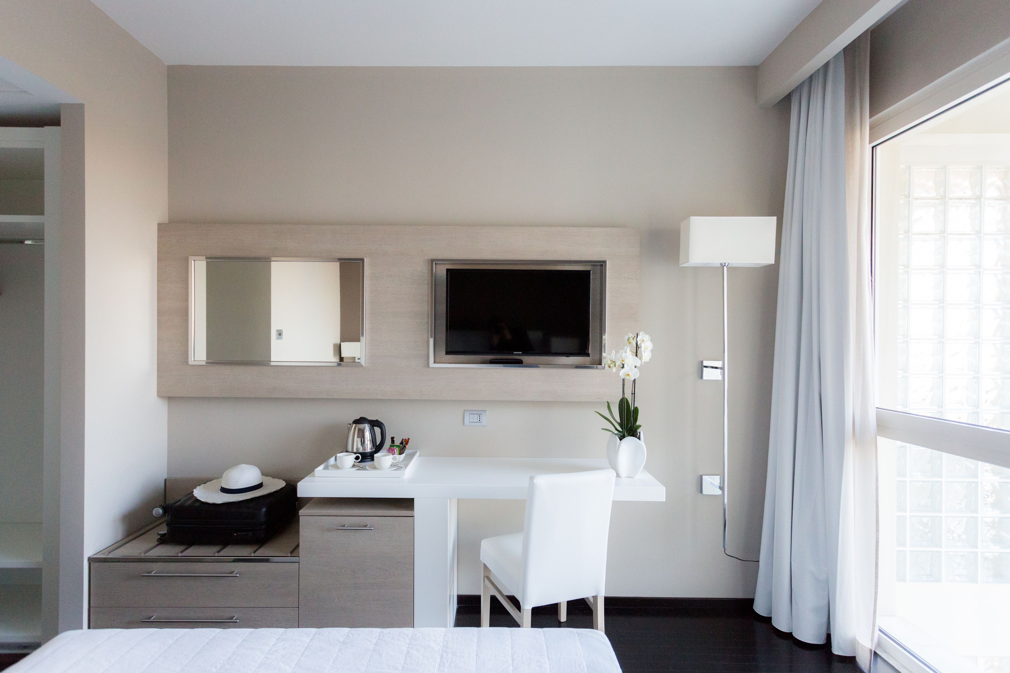 Una habitación de hotel moderna con una cama, un escritorio con una silla, un televisor, un espejo y una ventana con cortinas.