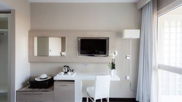 Una habitación de hotel moderna con una cama, un escritorio con una silla, un televisor, un espejo y una ventana con cortinas.