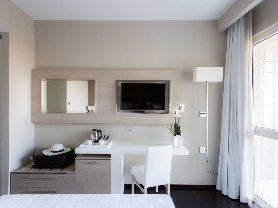 Una habitación de hotel moderna con una cama, un escritorio con una silla, un televisor, un espejo y una ventana con cortinas.