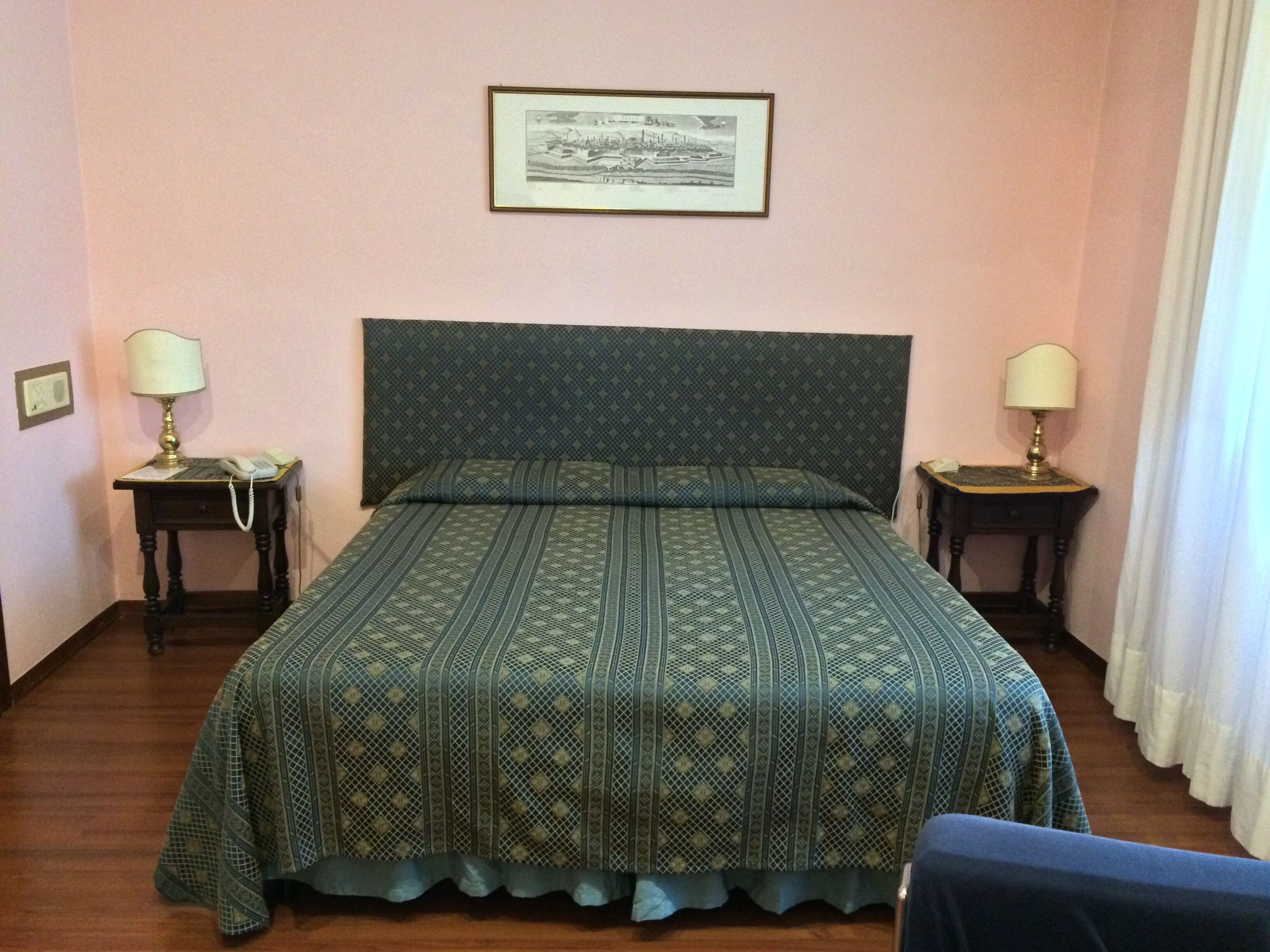 Una stanza con un letto, due comodini, un quadro appeso al muro e una finestra con tende.