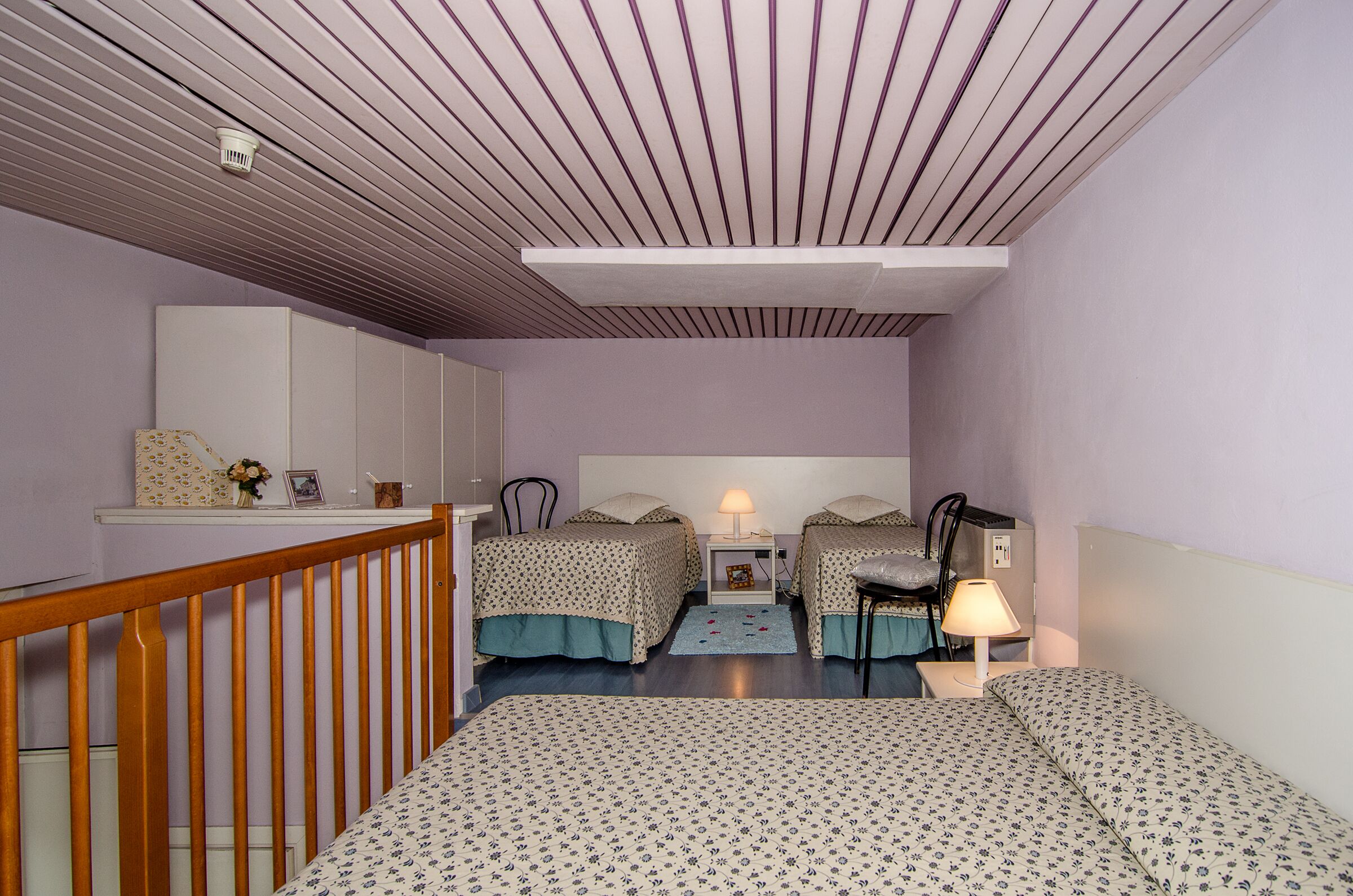 A bedroom with two beds, a wooden headboard, a nightstand with a lamp, and a mirror on the wall.