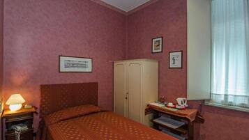 A room with a bed, a wardrobe, a desk with a lamp, and a window with curtains.