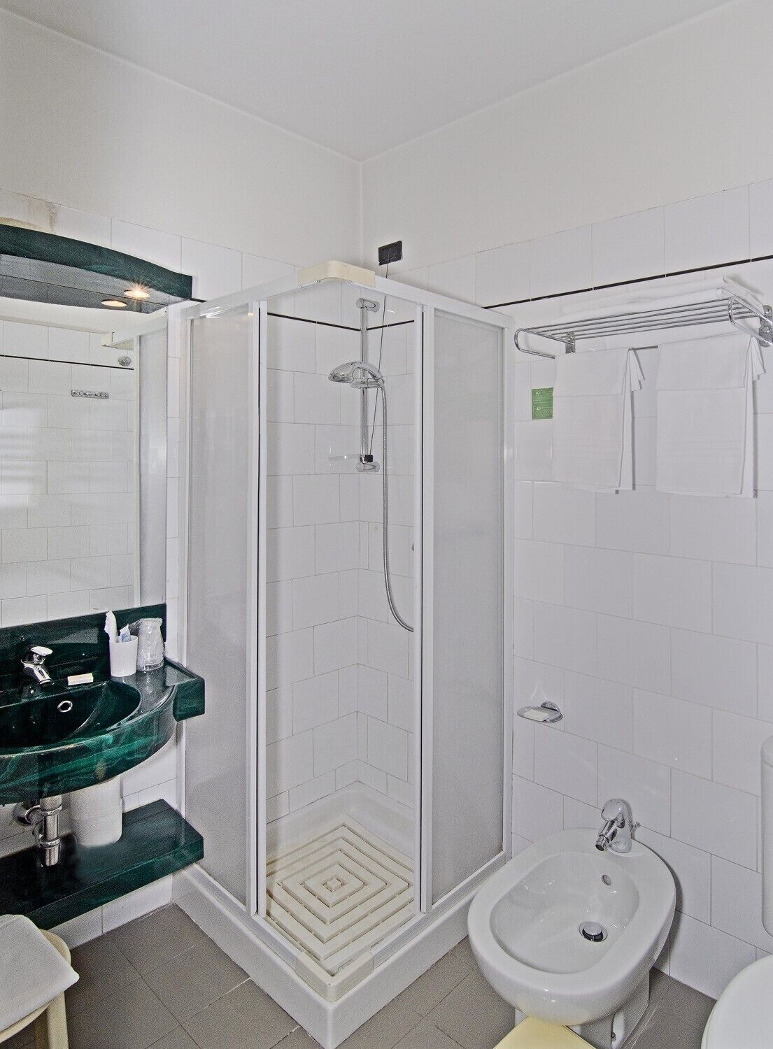 A bathroom with a glass-enclosed shower, a sink with a green countertop, and a bidet.