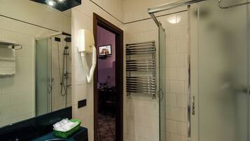 Un bagno con doccia, un lavandino con specchio, un portascopevoli e una televisione montata a parete.