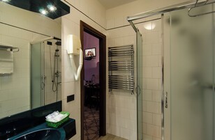 Un bagno con doccia, un lavandino con specchio, un portascopevoli e una televisione montata a parete.