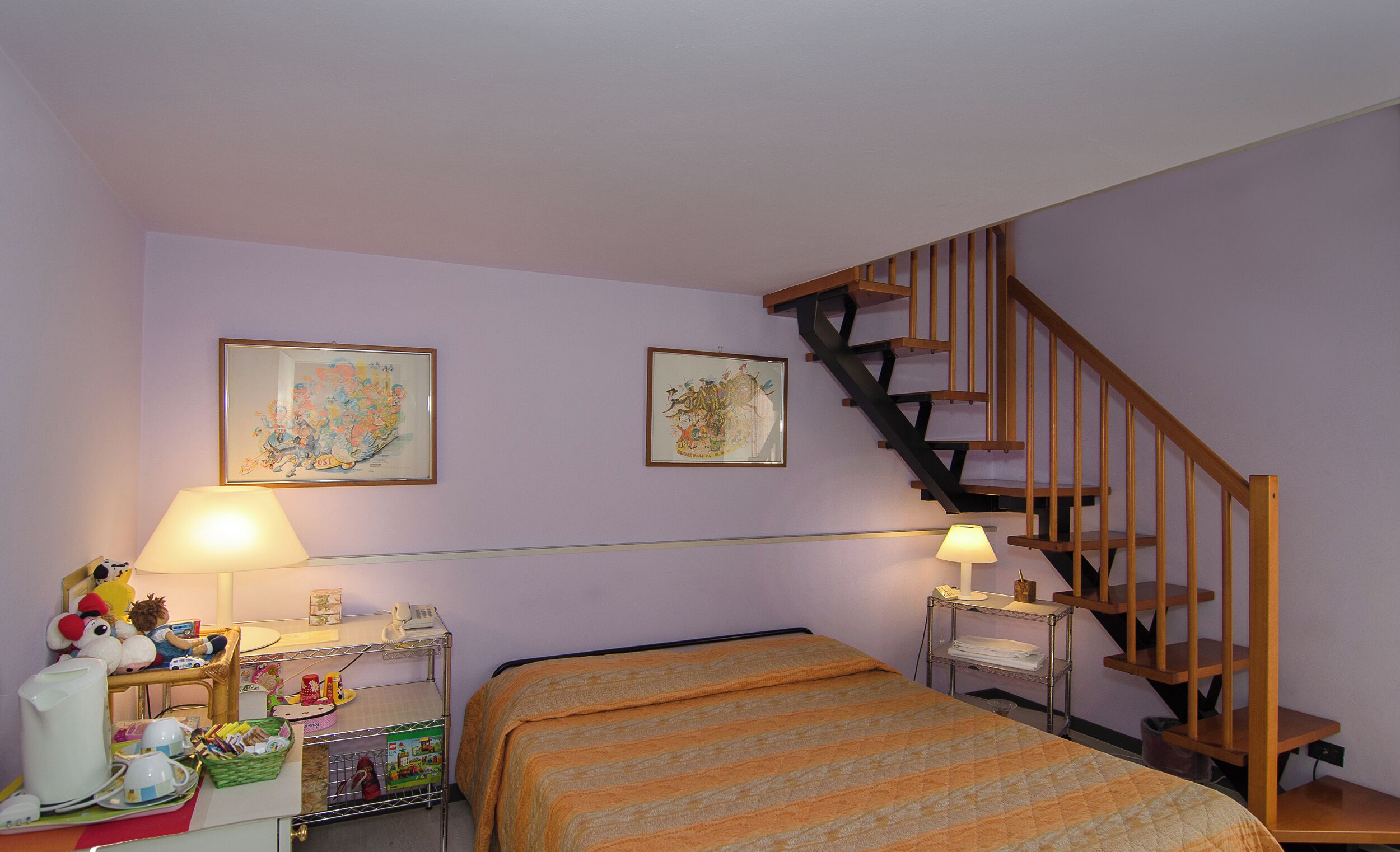 Un dormitorio con cama, mesita de noche, lámpara, silla, una pequeña mesa, estante y escalera.
