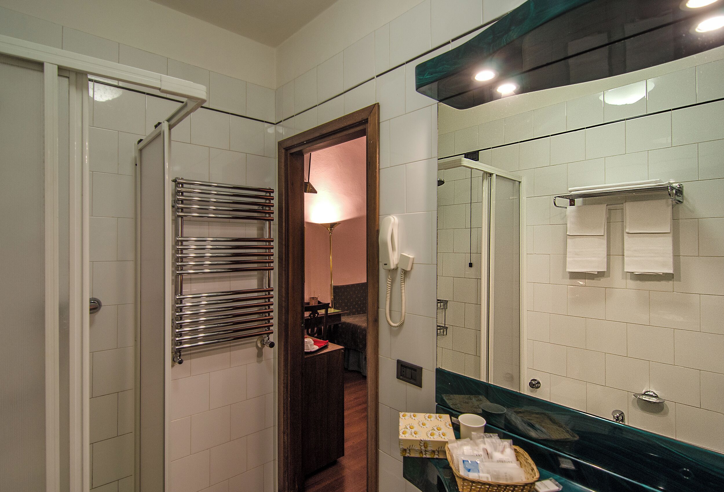 Un bagno d'albergo con cabina doccia in vetro, porta asciugamani, specchio e telefono.