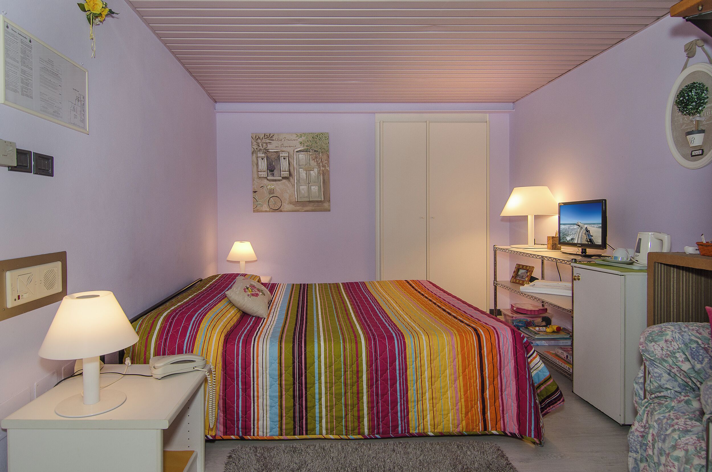 Un dormitorio con cama, lámparas de noche, un escritorio con computadora y cómoda.