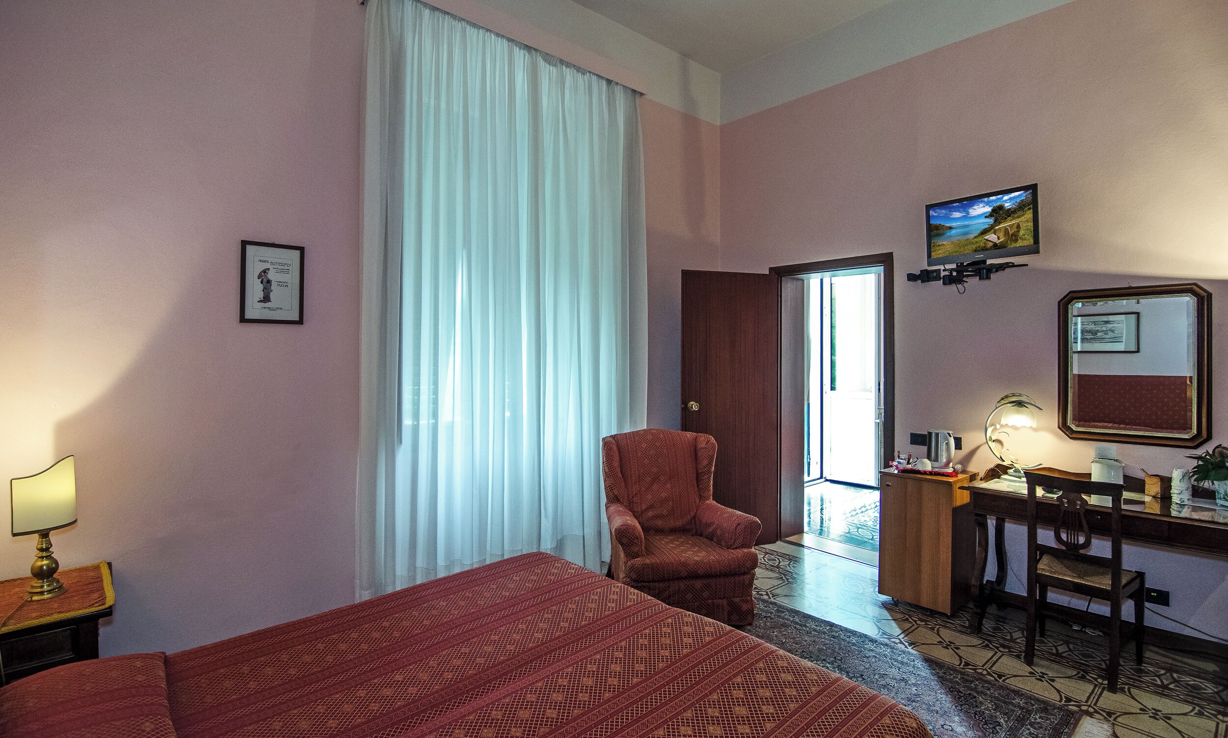 A hotel room with a bed, a chair, a desk, a television, and a large window with curtains.
