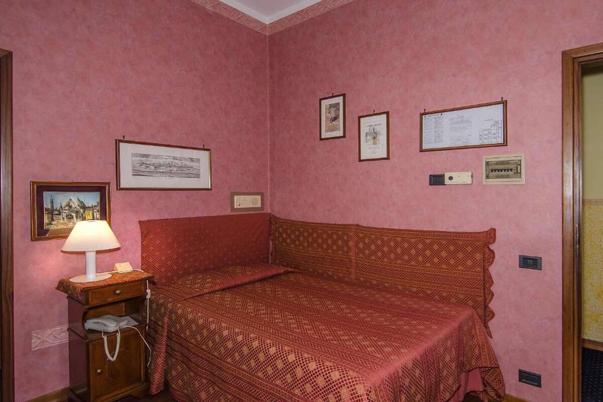 A room with a single bed, a nightstand with a lamp, and framed pictures on the wall.