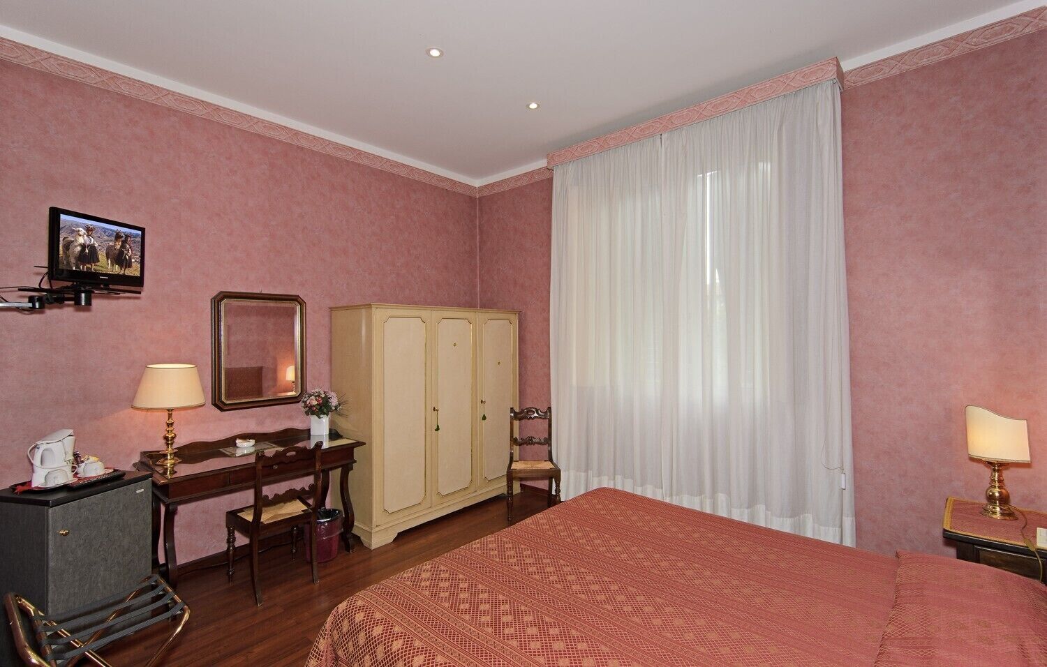 A hotel room with a bed, a desk, a wardrobe, a chair, and a television.