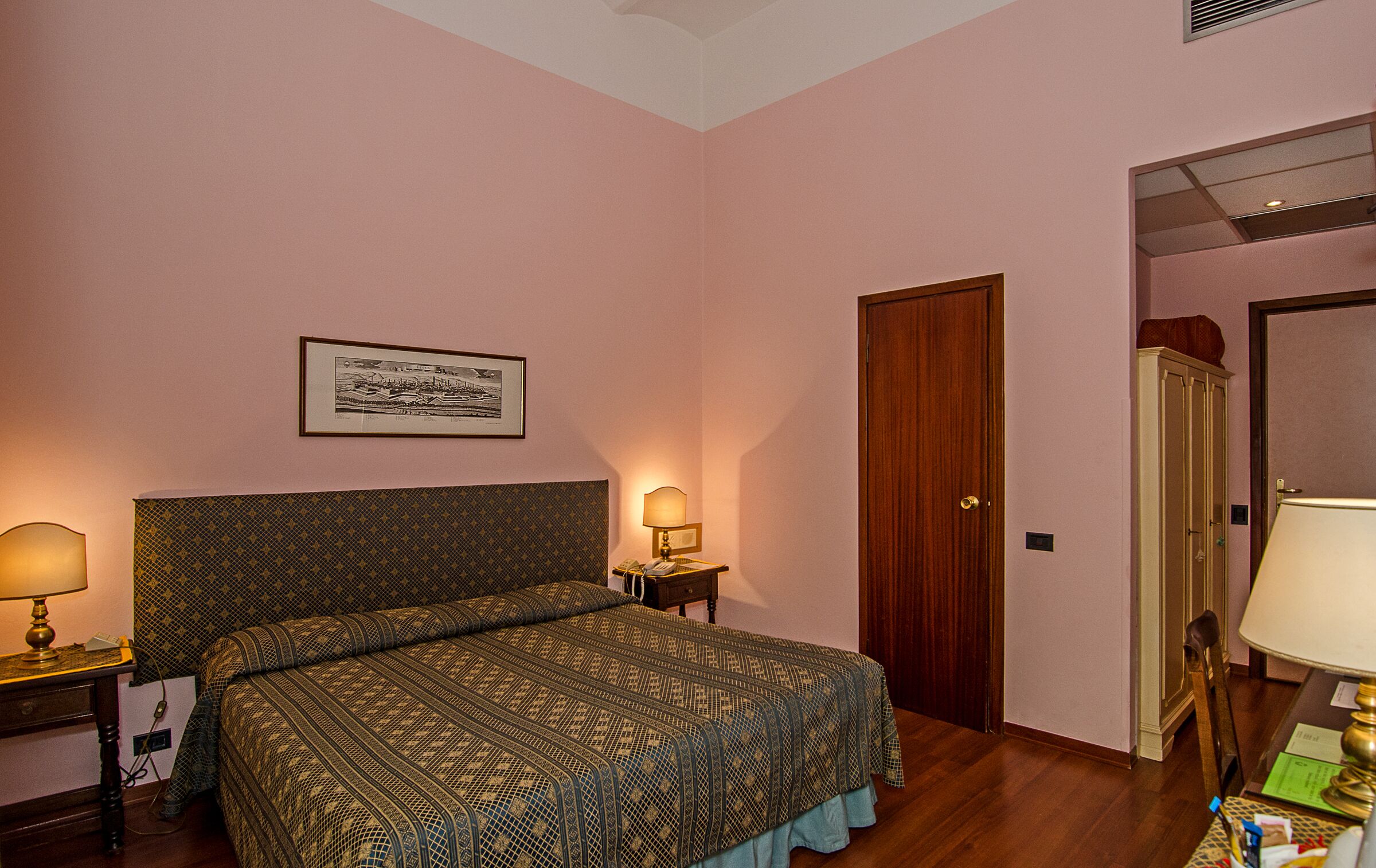 A hotel room with a bed, bedside tables, a lamp, a framed picture on the wall, and a door.