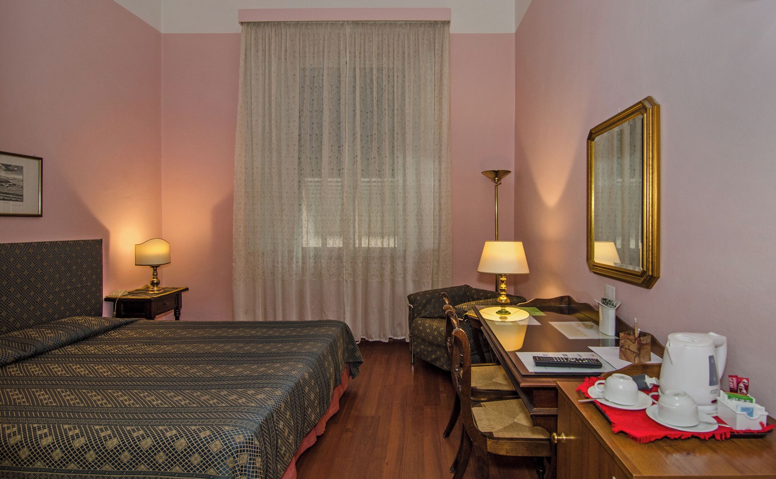 A hotel room with two beds, a desk with a chair, a table with a kettle, cups, and a coffee machine.