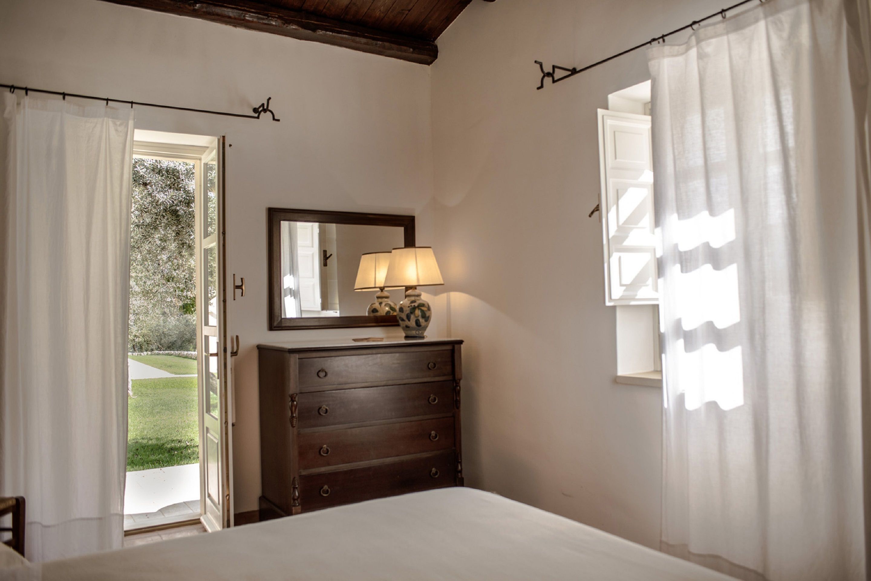 A bedroom with a bed, a dresser, a mirror, and a window with curtains.