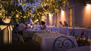 An outdoor dining area with tables set for a meal, surrounded by trees and illuminated by wall-mounted lights. - Hotel Masseria degli Ulivi (Noto)