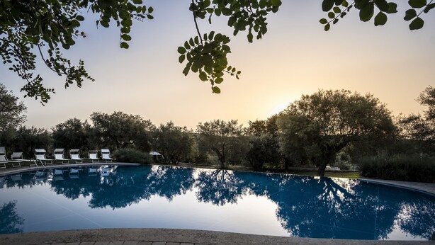 A swimming pool with lounge chairs and trees in the background. - Hotel Masseria degli Ulivi (Noto)
