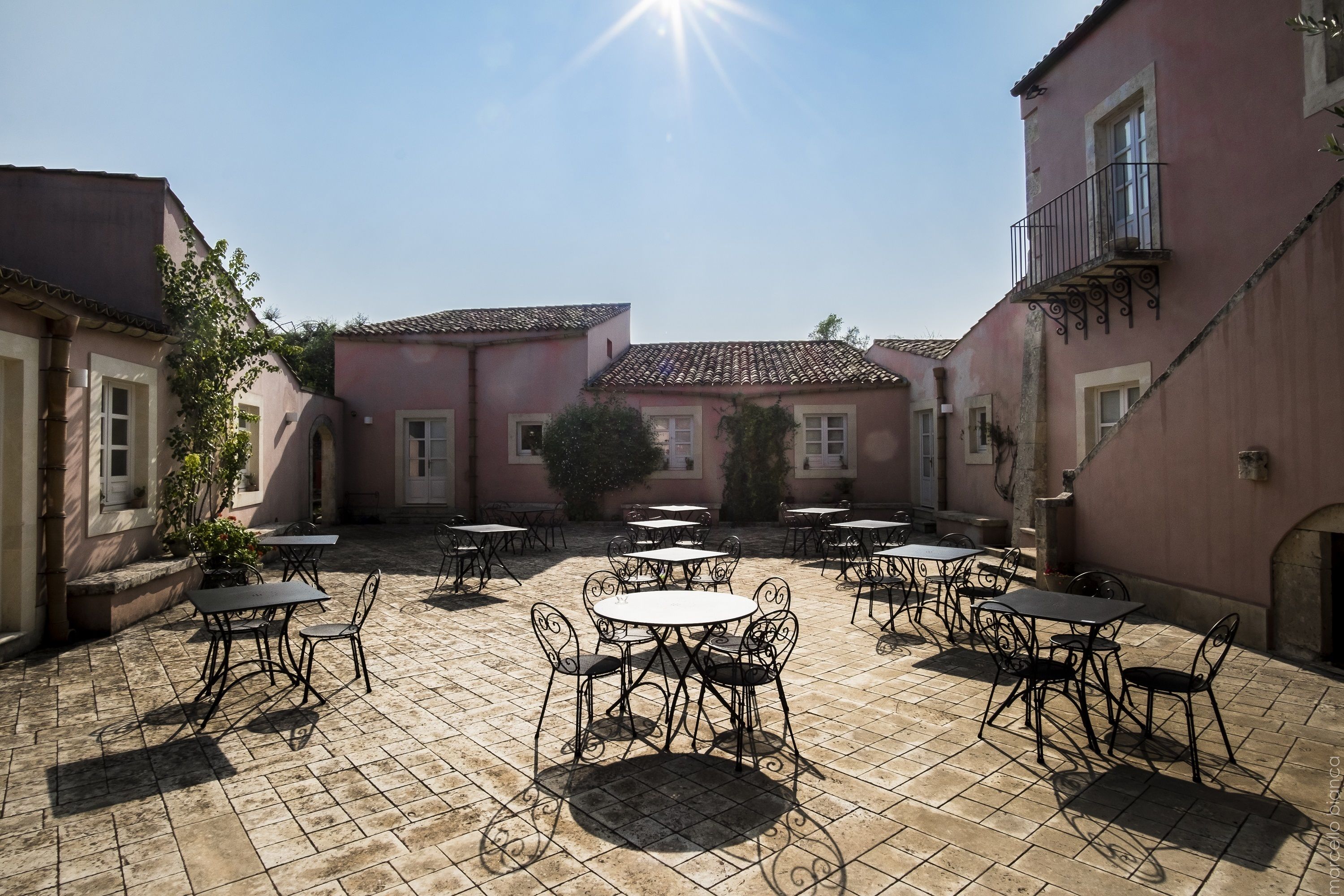 A courtyard with outdoor tables and chairs, surrounded by buildings with balconies and windows.