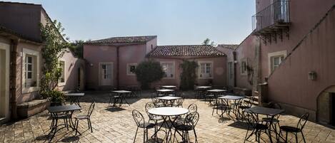 A courtyard with outdoor tables and chairs, surrounded by buildings with balconies and windows.