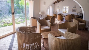 A spacious room with wicker furniture, large windows, and a stone wall view. - Hotel Masseria degli Ulivi (Noto)
