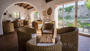 A spacious patio area with wicker furniture, a wooden coffee table, and a stone wall in the background. - Hotel Masseria degli Ulivi (Noto)