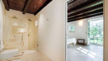 A modern bathroom with a glass shower, a toilet, and a sink. There is a door leading to a balcony with a table and chairs.
