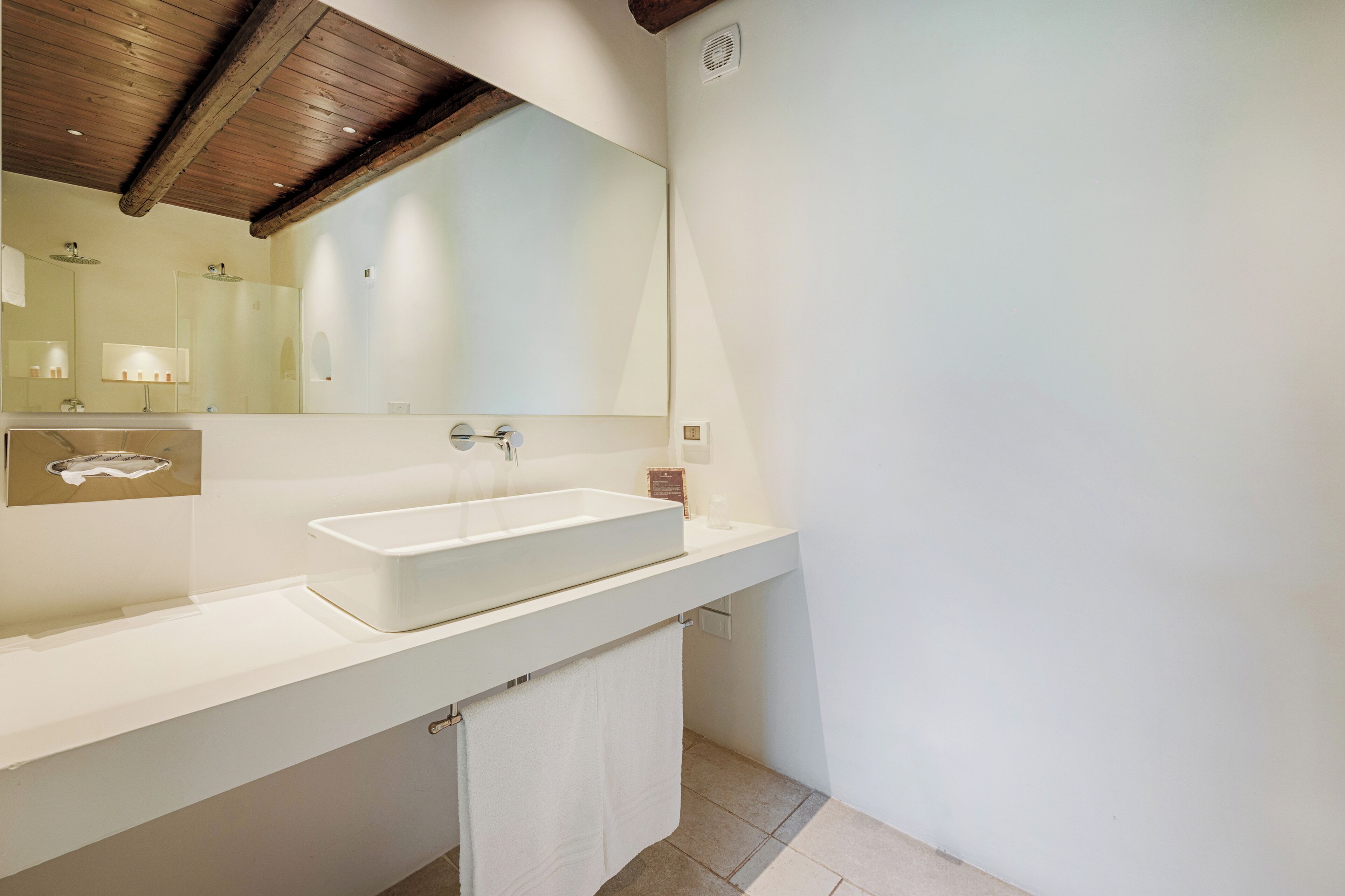 Un bagno moderno con uno specchio grande, un lavabo rettangolare e un asciugamano appeso al muro.